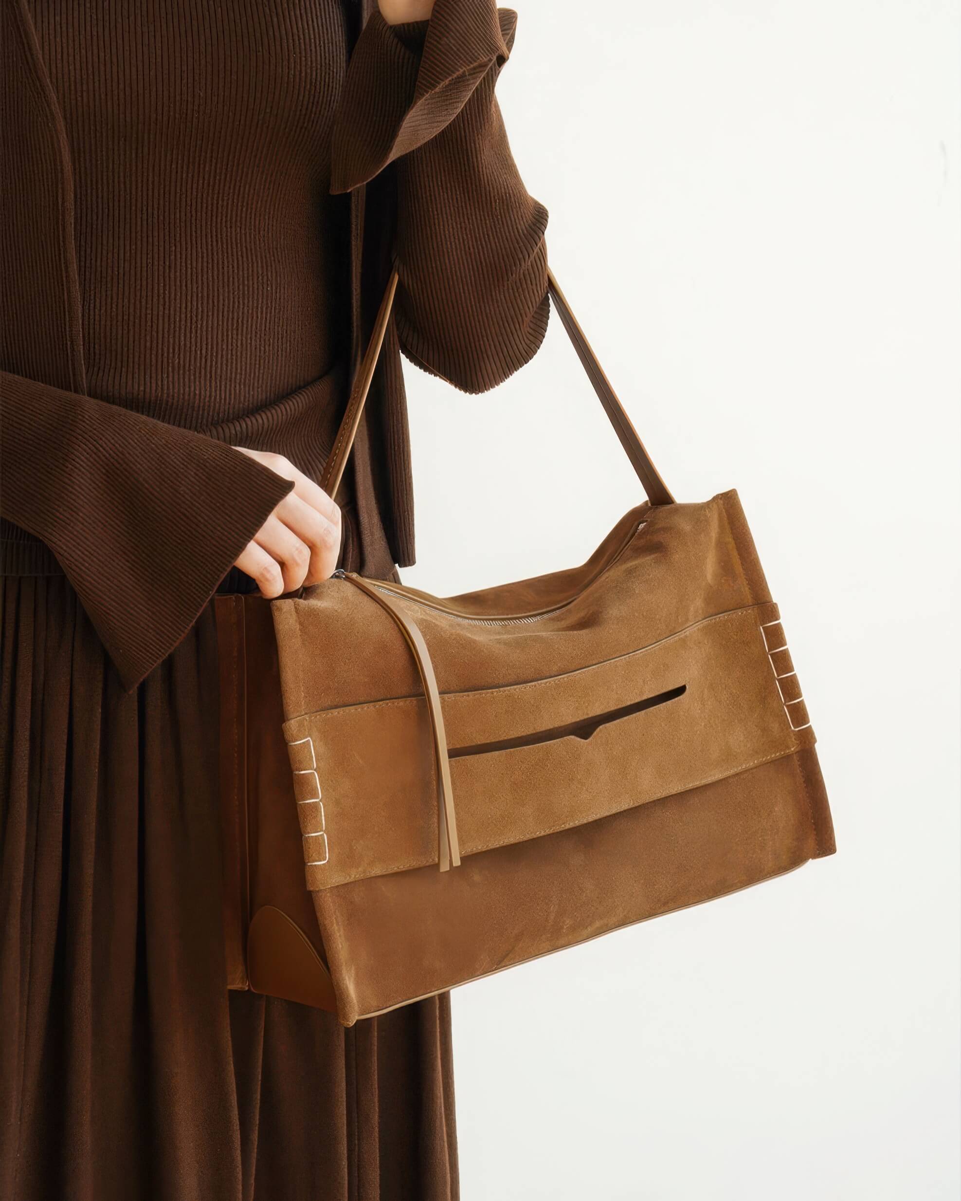 Side view of the minimalist suede shoulder bag in brown, highlighting the textured material, top zipper, and decorative side stitching.