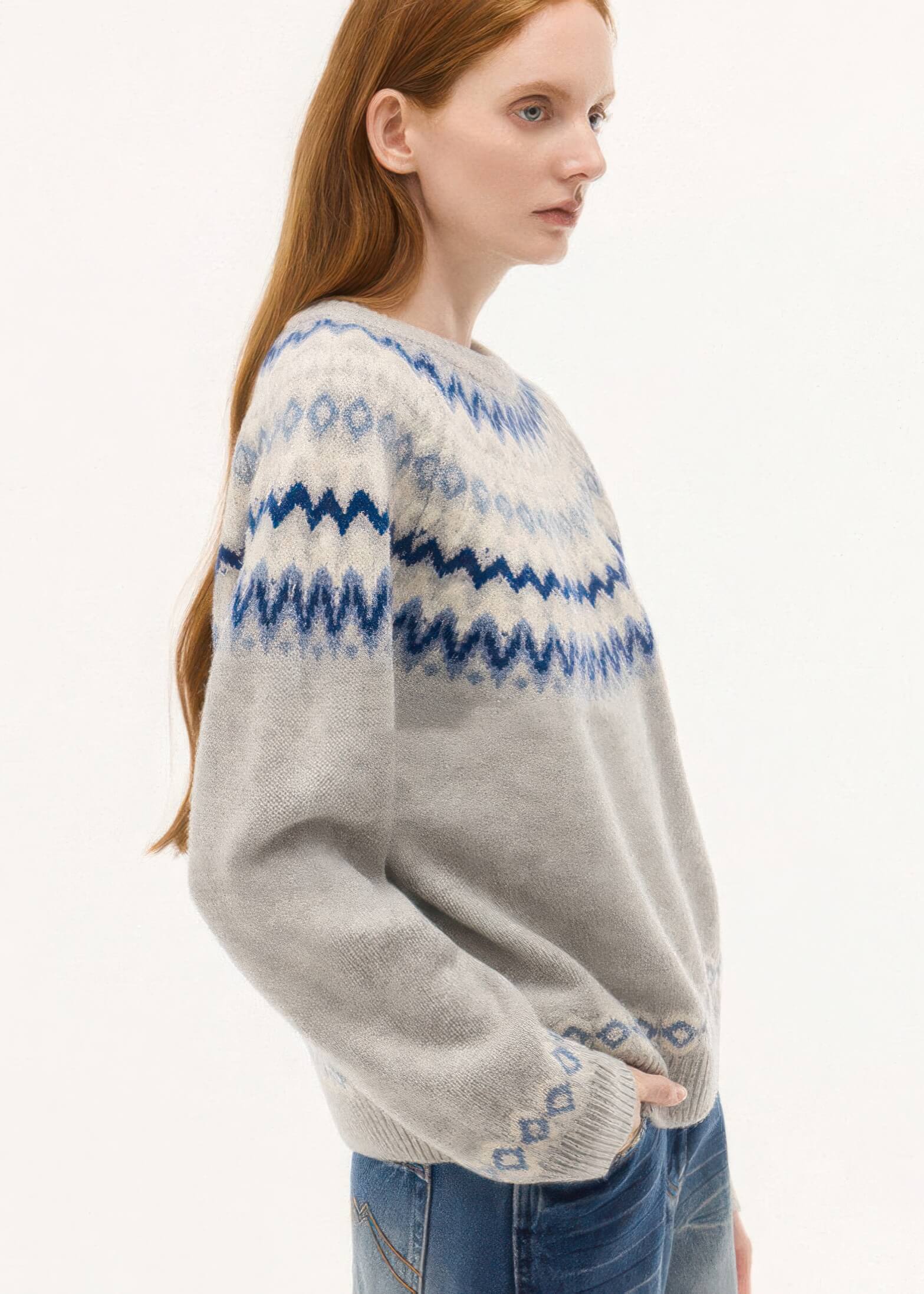 A side profile shot of the model highlighting the continuous blue geometric pattern across the shoulders and the relaxed, slightly oversized fit of the grey knit.