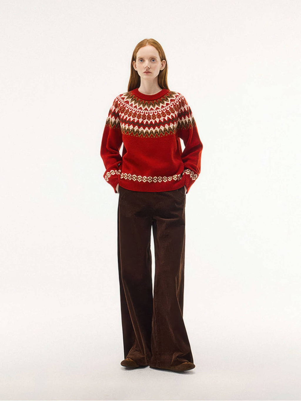 A full-length studio shot of the red Nordic knit sweater. The model has her hands in the pockets of her wide-leg brown corduroy pants, emphasizing a warm, autumnal aesthetic.