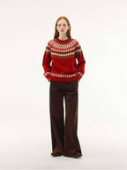 A full-length studio shot of the red Nordic knit sweater. The model has her hands in the pockets of her wide-leg brown corduroy pants, emphasizing a warm, autumnal aesthetic.