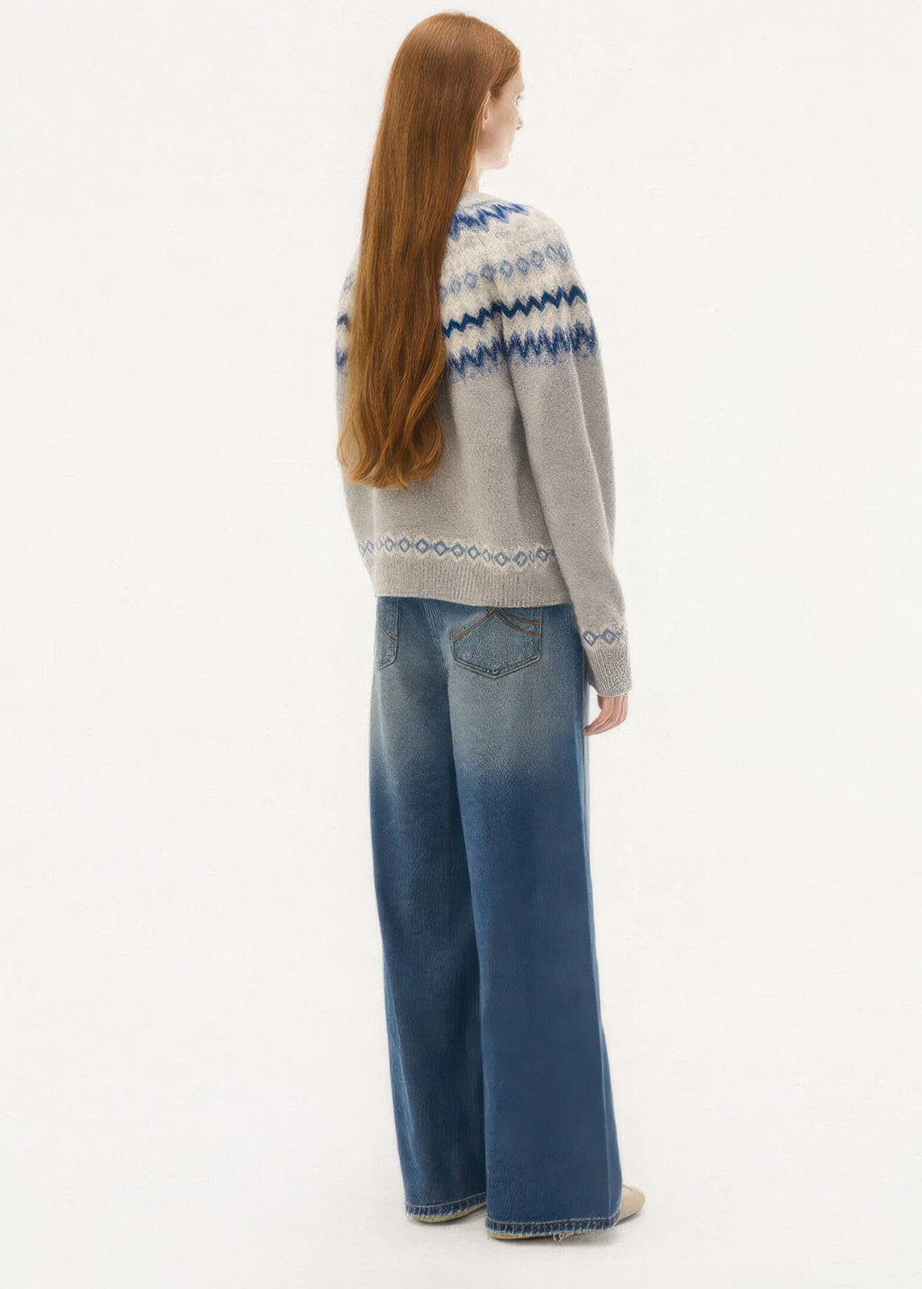 A full-length back view showing the Nordic pattern wrapping entirely around the yoke and hem, styled with loose-fitting, faded blue jeans.
