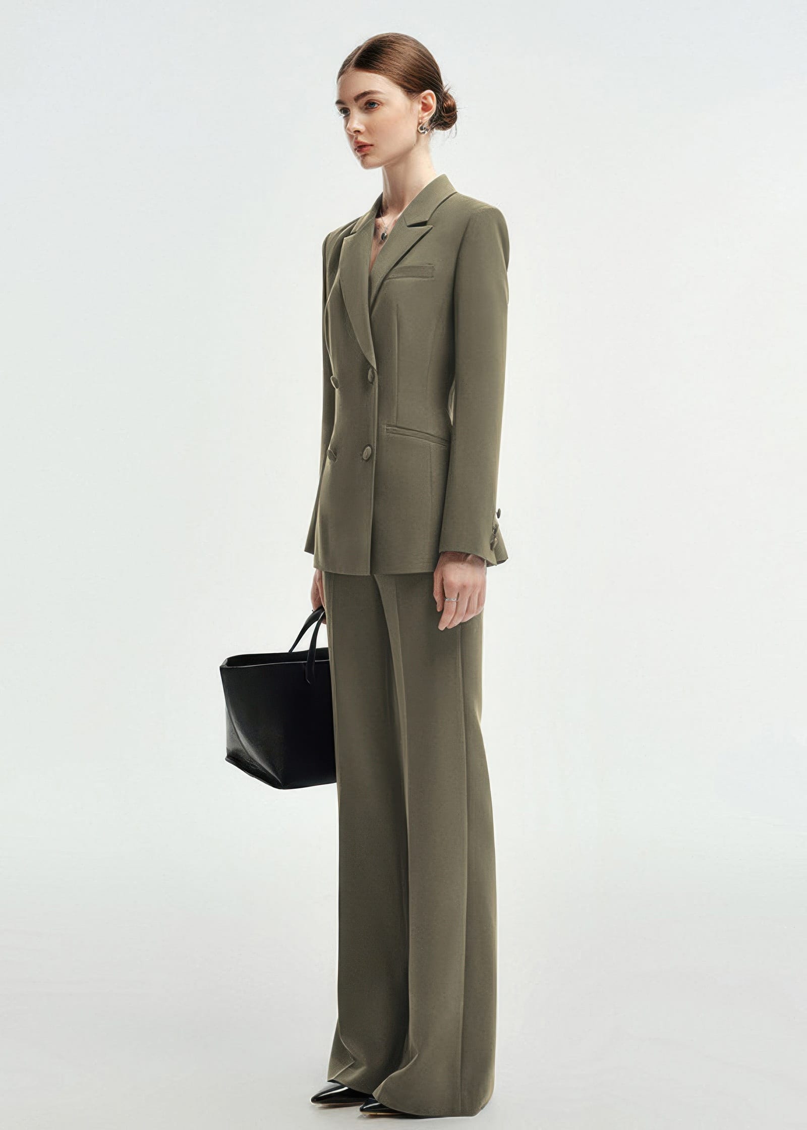 A side profile view of a woman in an olive green double-breasted tailored pantsuit with wide-leg trousers.
