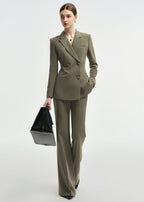 A woman walking forward in an olive green double-breasted tailored pantsuit, carrying a black leather tote bag in her right hand.