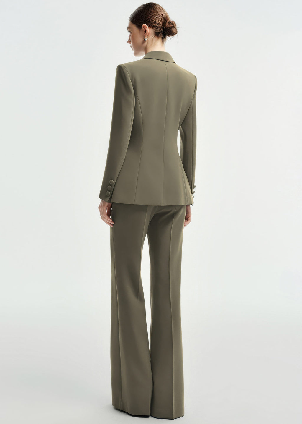 A rear view of a woman wearing an olive green tailored pantsuit, highlighting the structured back of the blazer and the fit of the wide-leg trousers.