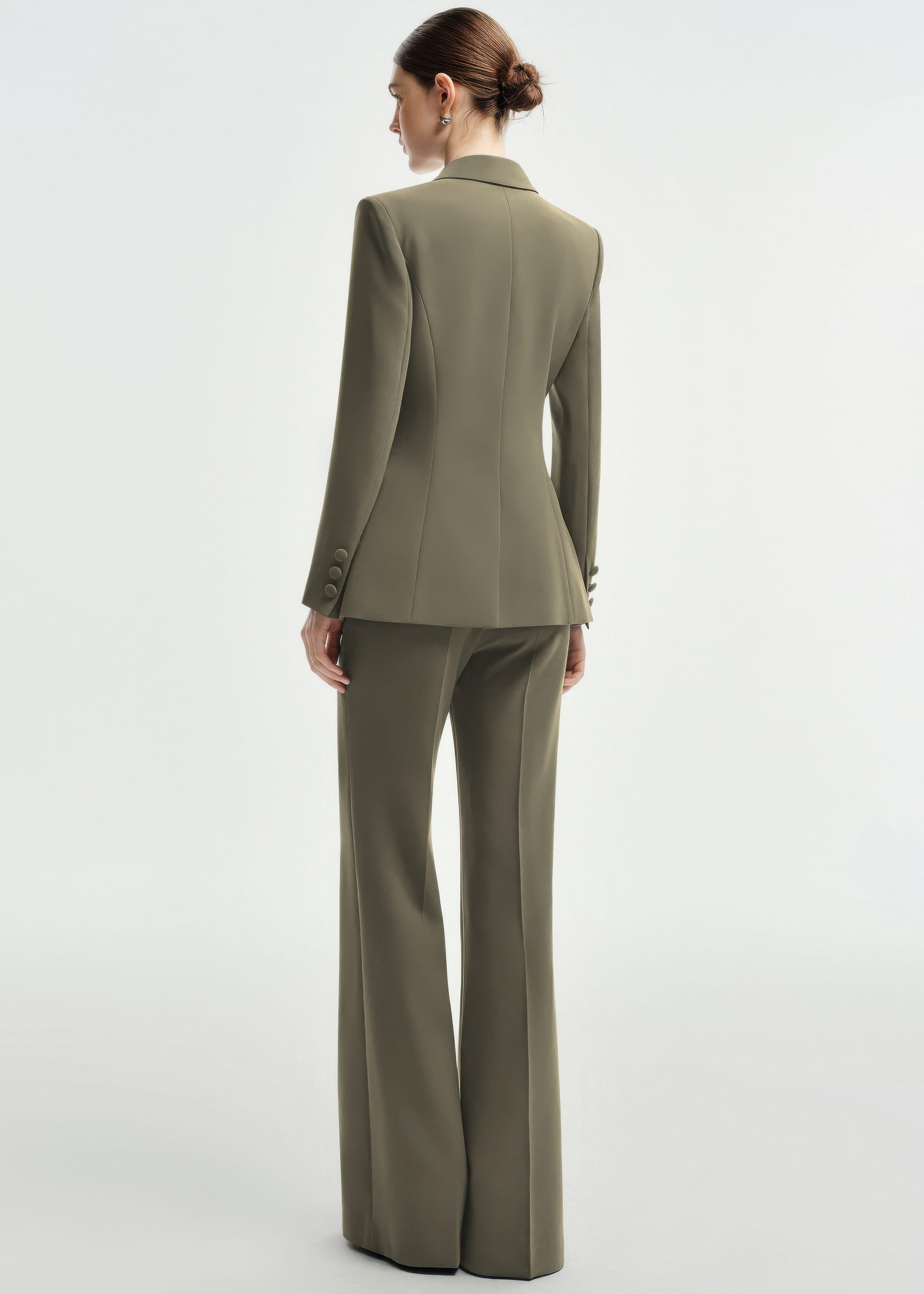 A rear view of a woman wearing an olive green tailored pantsuit, highlighting the structured back of the blazer and the fit of the wide-leg trousers.