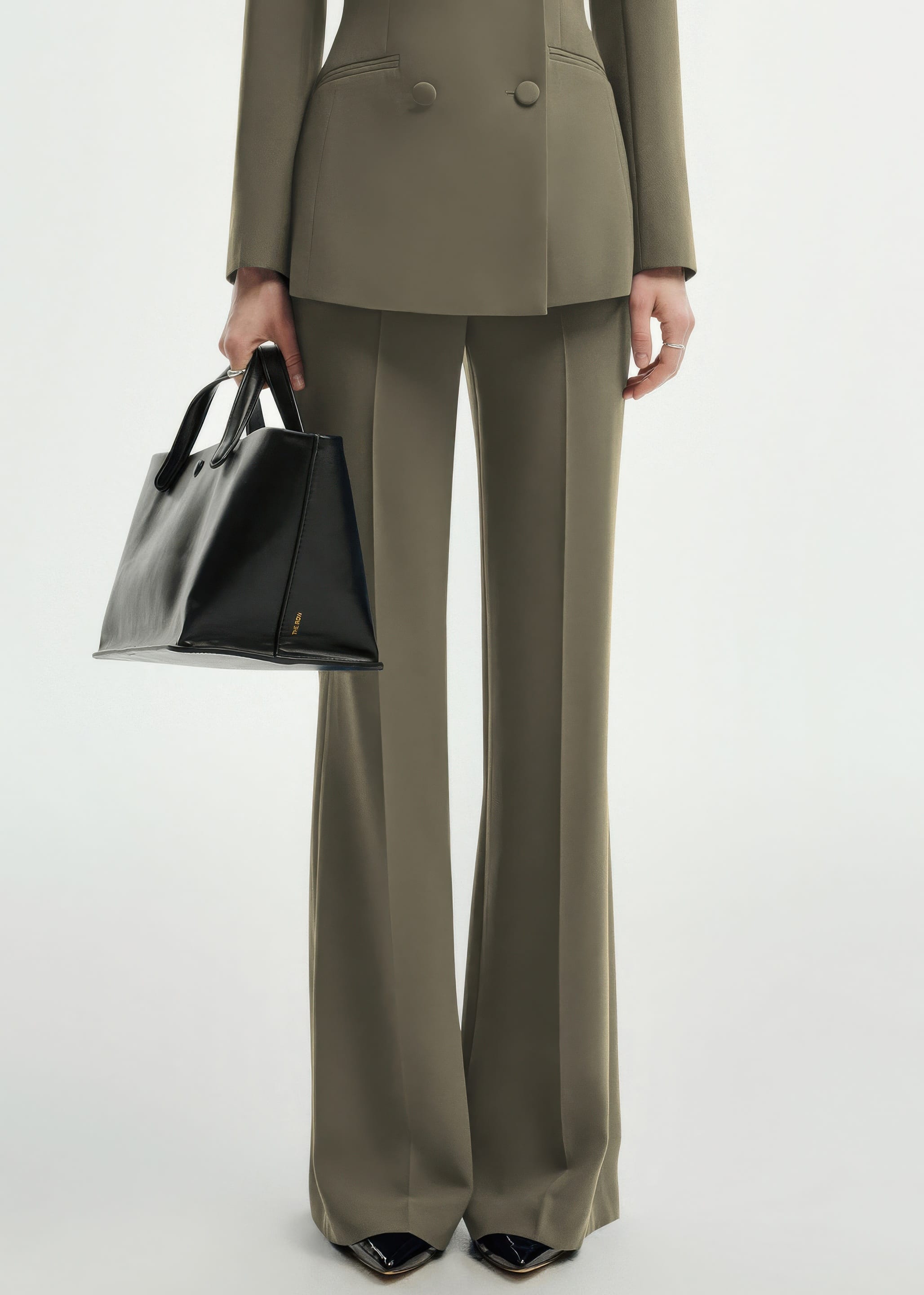 A close-up shot focusing on the lower half of the olive green pantsuit, showing the tailored trousers and a black leather handbag.