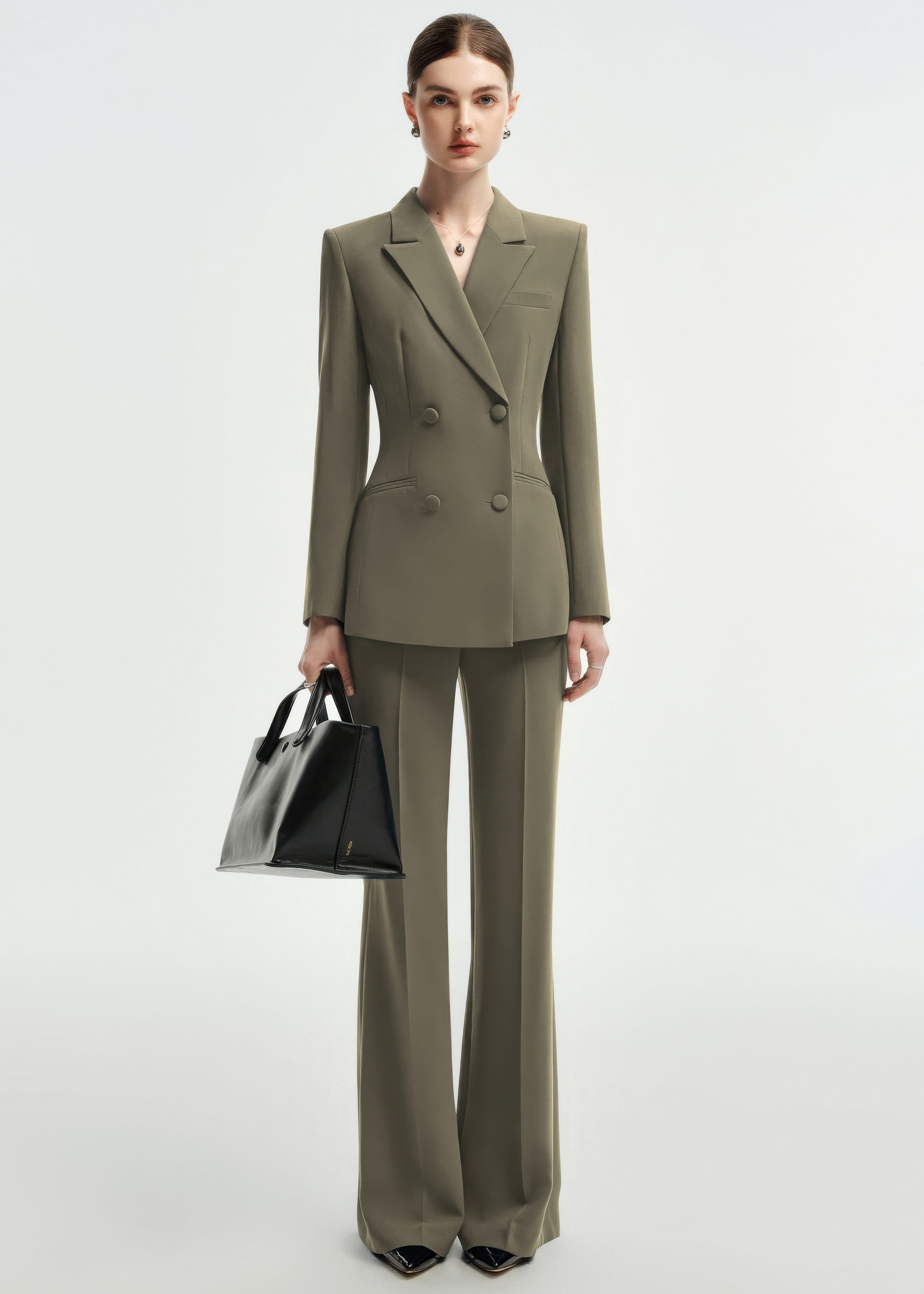 A full-length front view of a woman standing in an olive green double-breasted tailored pantsuit.