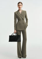 A full-length view of a woman posing in an olive green double-breasted tailored pantsuit with one hand in her pocket.