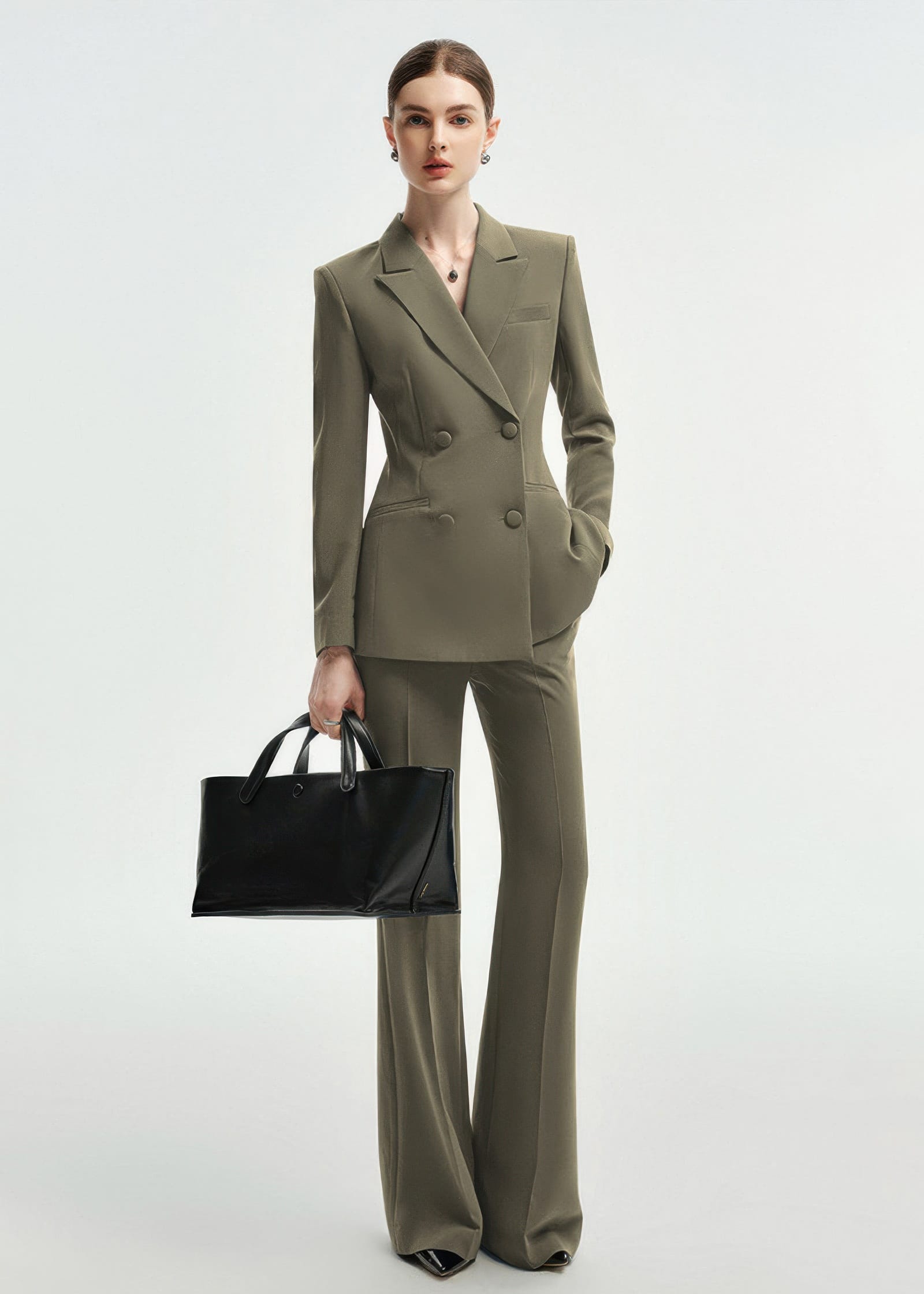 A full-length view of a woman posing in an olive green double-breasted tailored pantsuit with one hand in her pocket.