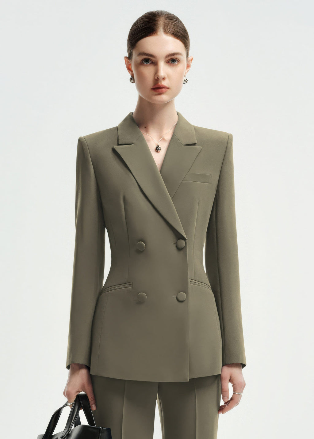 A medium shot of a woman wearing an olive green double-breasted tailored blazer, showcasing the lapel and button details.