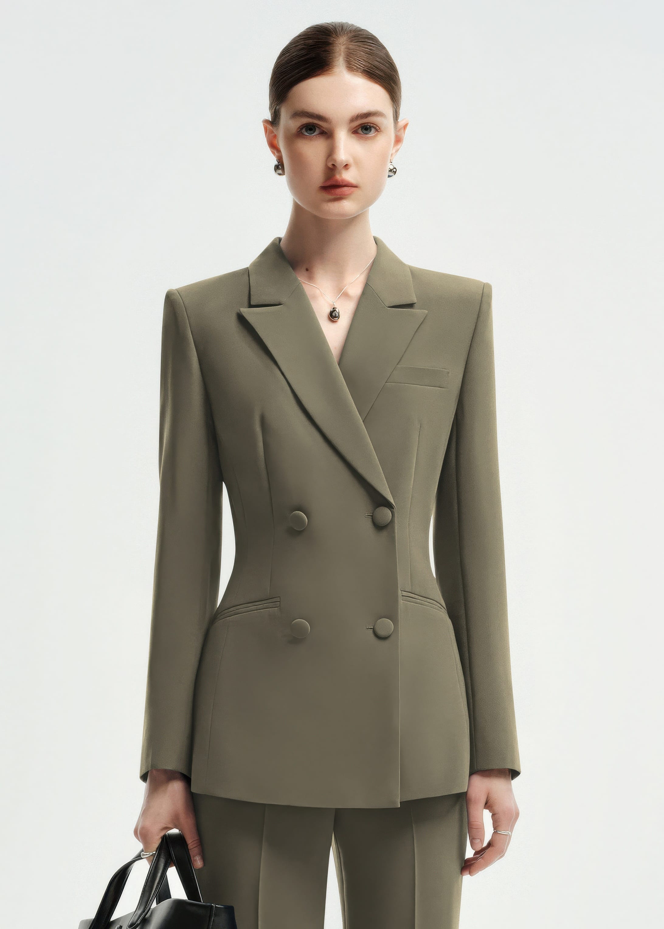 A medium shot of a woman wearing an olive green double-breasted tailored blazer, showcasing the lapel and button details.