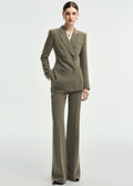 A full-body shot of a woman in an olive green double-breasted tailored pantsuit, standing against a plain white background.