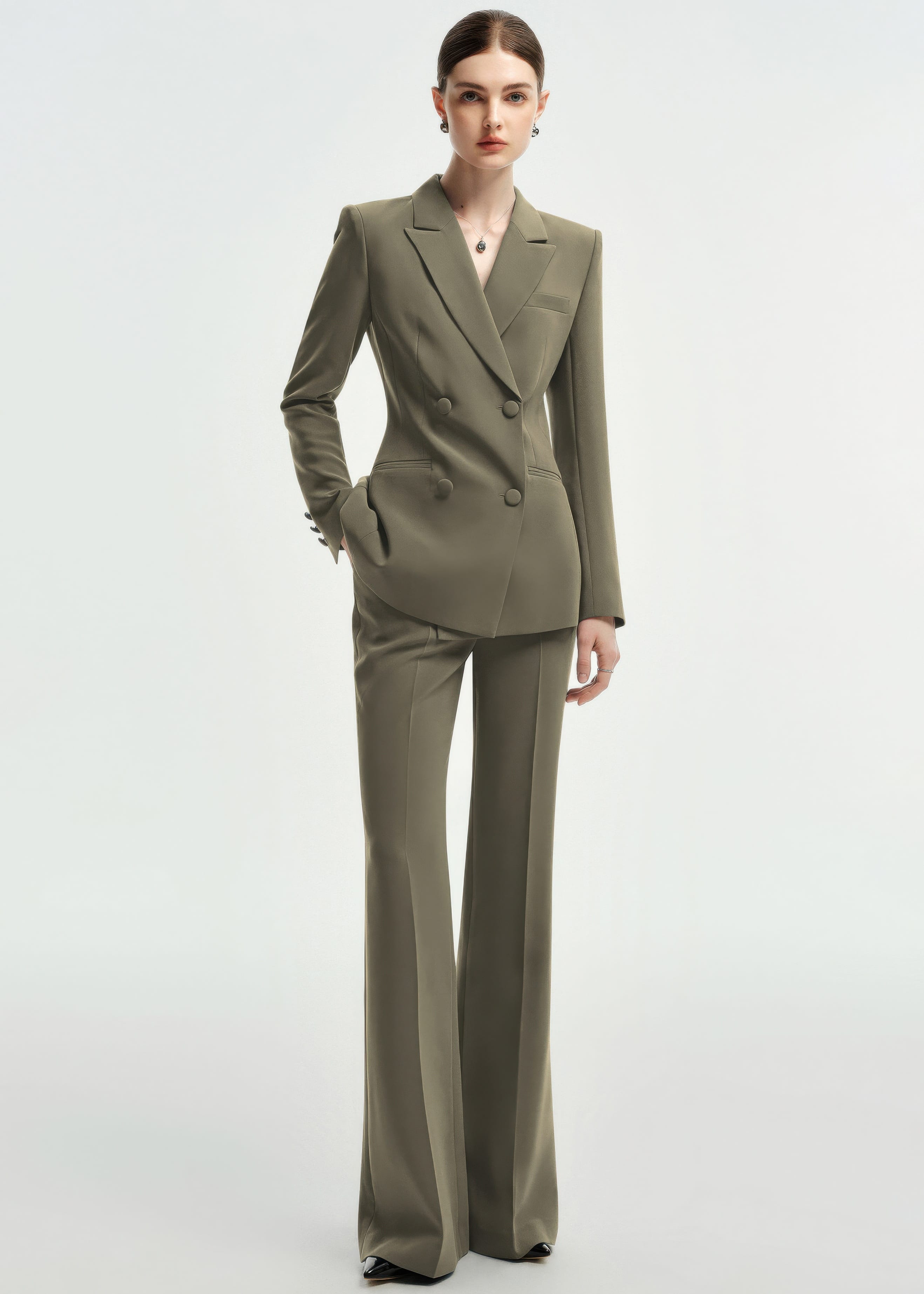 A full-body shot of a woman in an olive green double-breasted tailored pantsuit, standing against a plain white background.