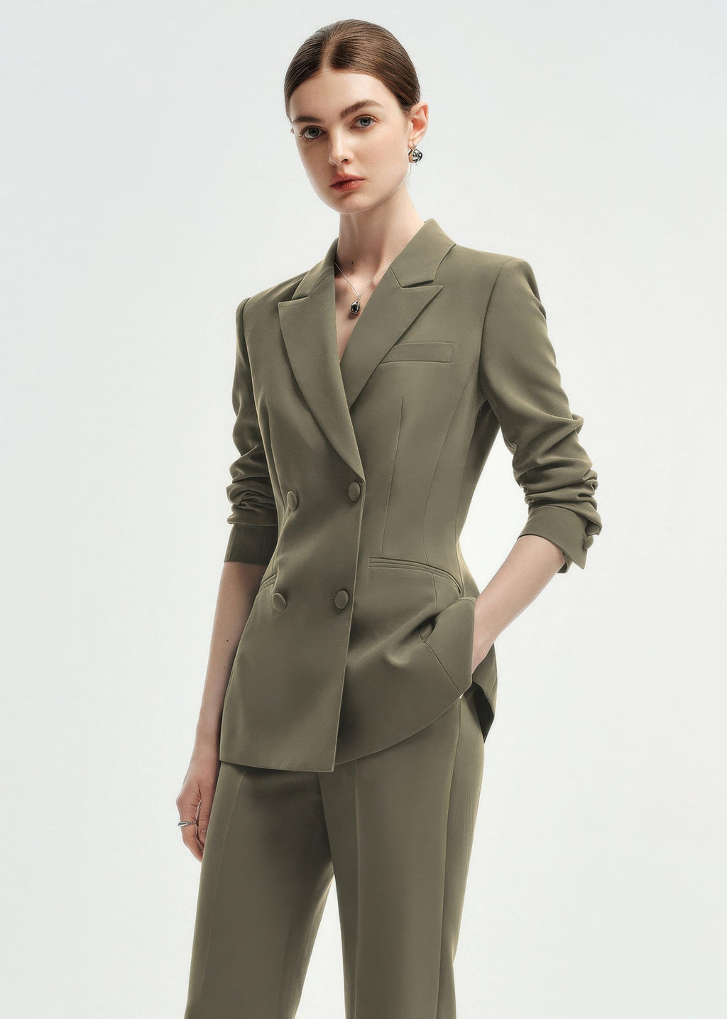 A three-quarter view of a woman in an olive green double-breasted tailored blazer with the sleeves slightly pushed up.