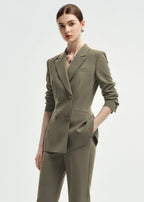 A three-quarter view of a woman in an olive green double-breasted tailored blazer with the sleeves slightly pushed up.