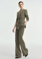A full-length dynamic pose of a woman wearing an olive green double-breasted tailored pantsuit.