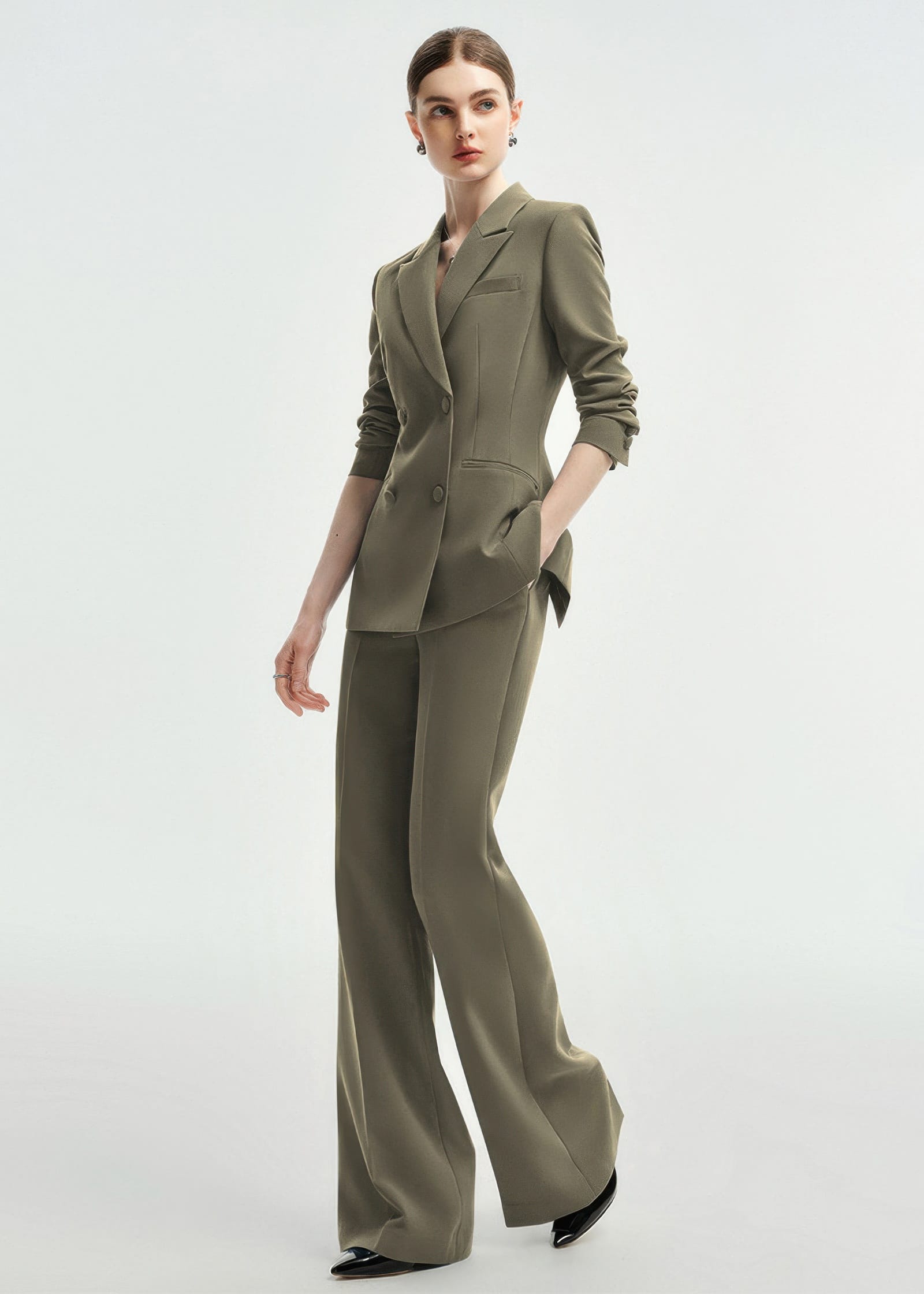 A full-length dynamic pose of a woman wearing an olive green double-breasted tailored pantsuit.