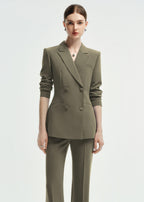 A front-facing medium shot of a woman in an olive green double-breasted tailored pantsuit, highlighting the structured shoulders and fit.