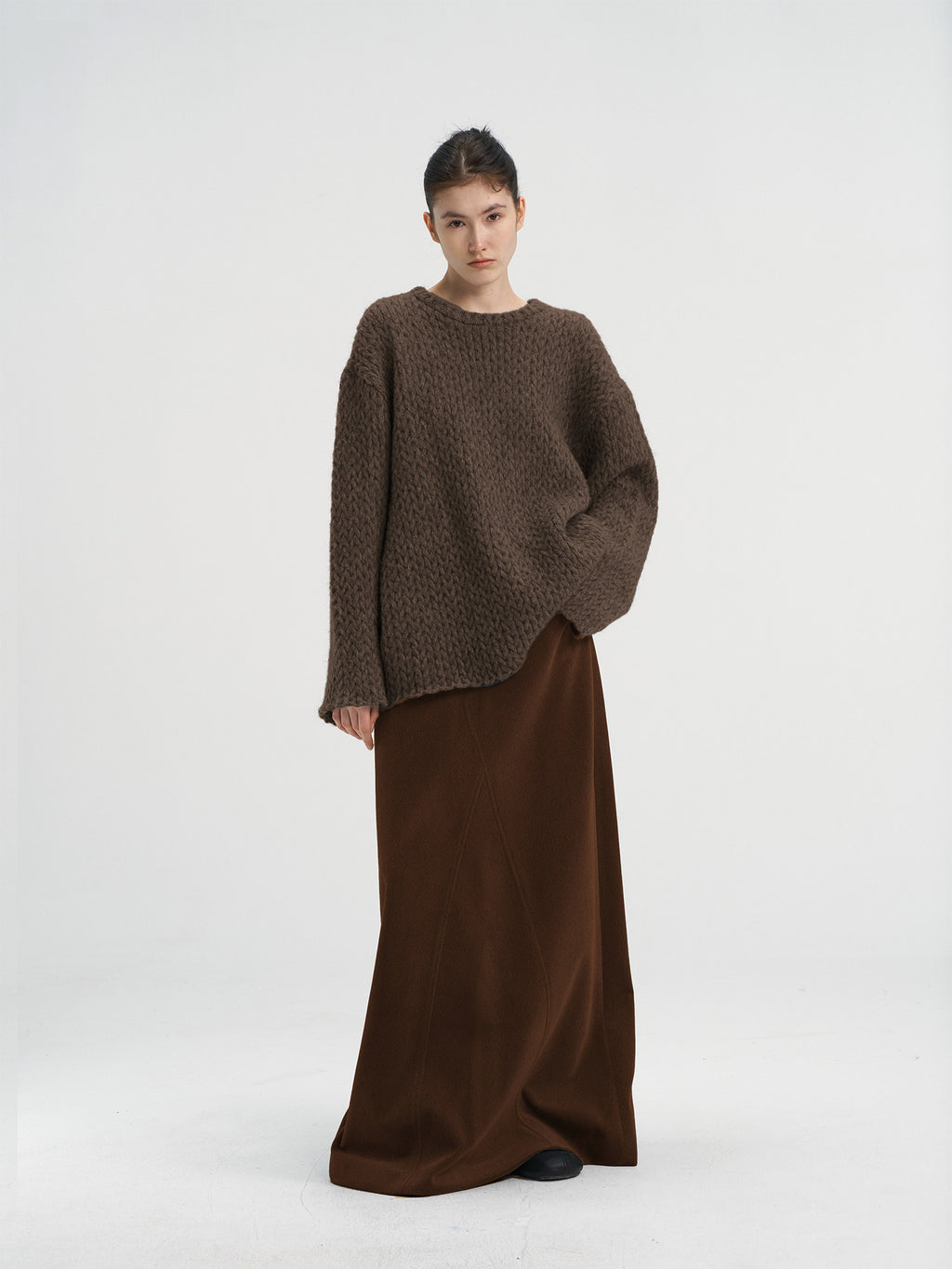 Full-length shot of a brown chunky knit wool sweater paired with a dark brown long skirt, minimalist winter outfit for women.