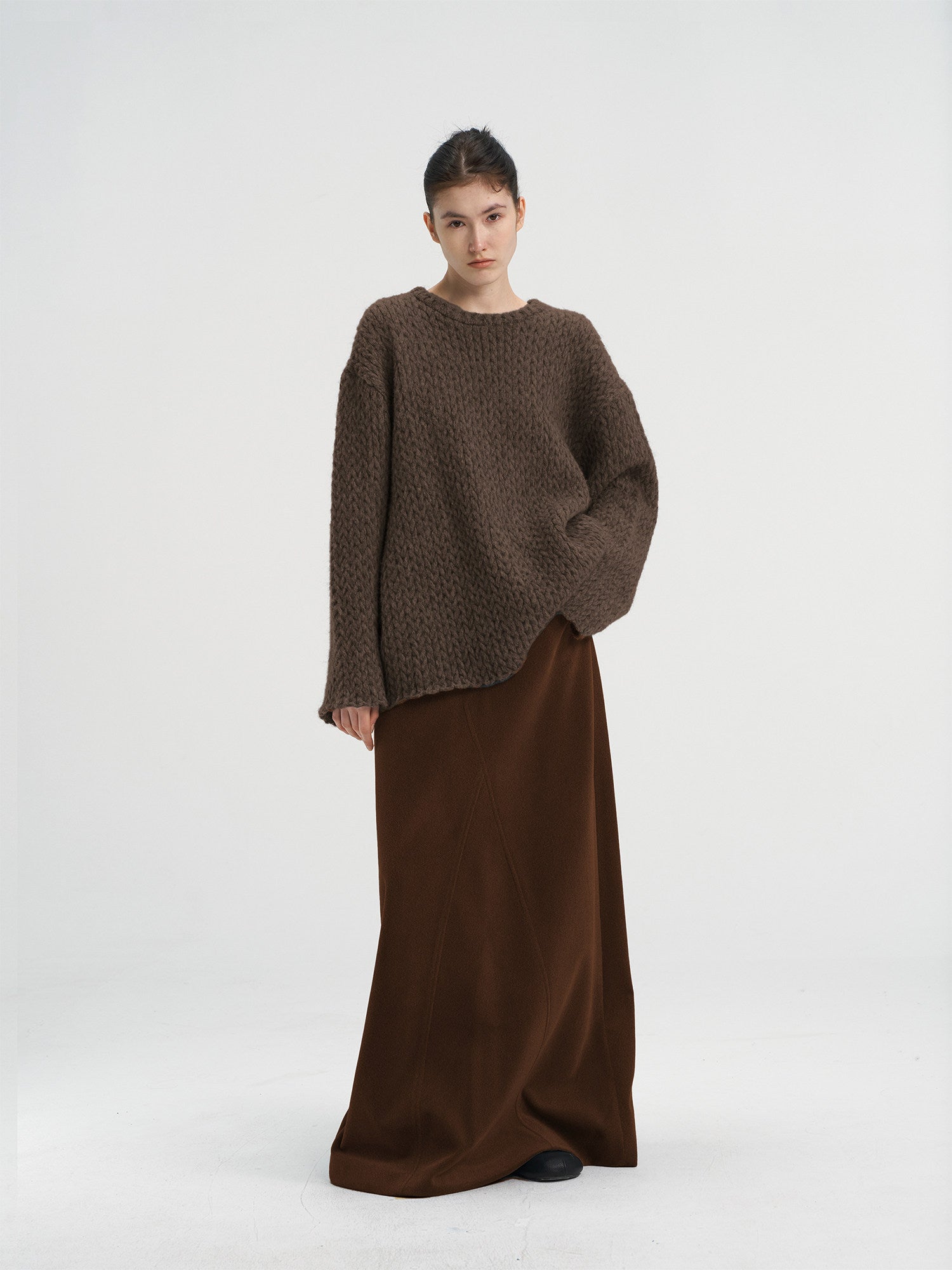 Full-length shot of a brown chunky knit wool sweater paired with a dark brown long skirt, minimalist winter outfit for women.