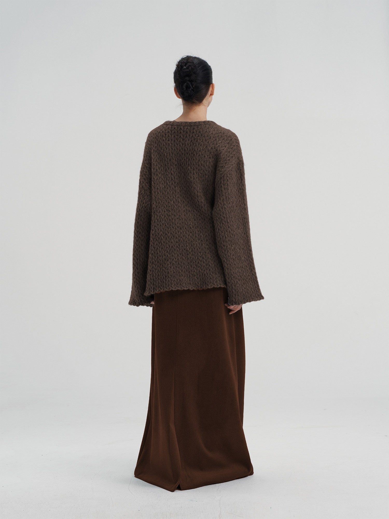 Rear view of a women's oversized brown wool knit pullover, showing the thick, textured weave and loose fit.