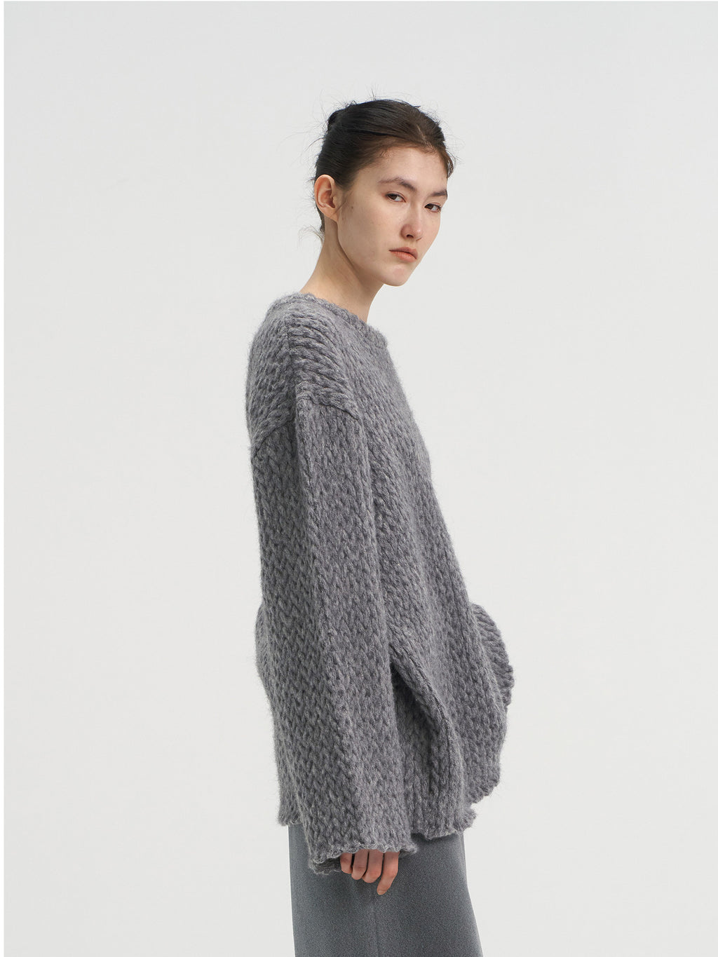 Side profile of a grey loose-fit chunky knit wool sweater for women, highlighting the thick texture and relaxed sleeve design.
