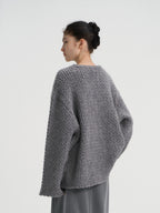 Back view of a women's oversized grey wool sweater featuring a chunky knit pattern and comfortable drop shoulder design.