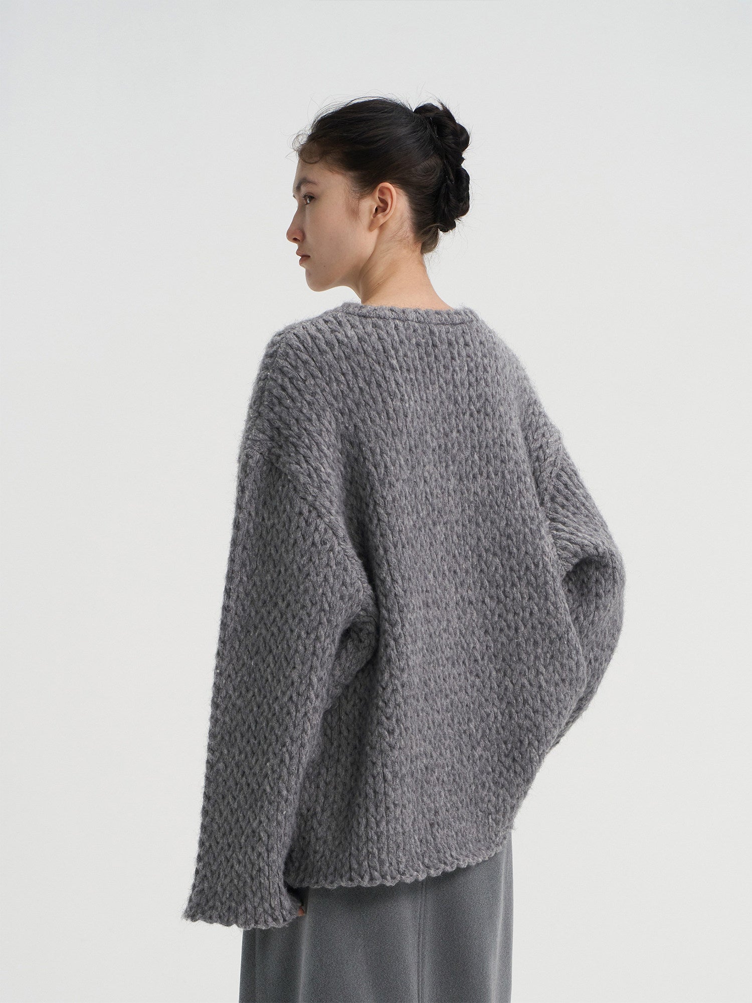 Back view of a women's oversized grey wool sweater featuring a chunky knit pattern and comfortable drop shoulder design.