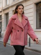 Model walking on a street wearing a dusty pink shearling wool double-breasted pea coat