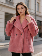 Close-up of a model adjusting the collar of a dusty pink double-breasted shearling pea coat