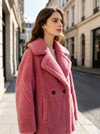Side profile angle of a model wearing a dusty pink shearling wool pea coat in an urban street setting