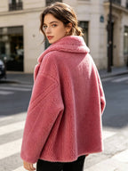 Back three-quarter angle view of a model wearing a dusty pink shearling wool pea coat looking over her shoulder