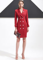 A full-length shot of a woman in a red shawl lapel blazer dress, holding a clutch and wearing light-colored heels.