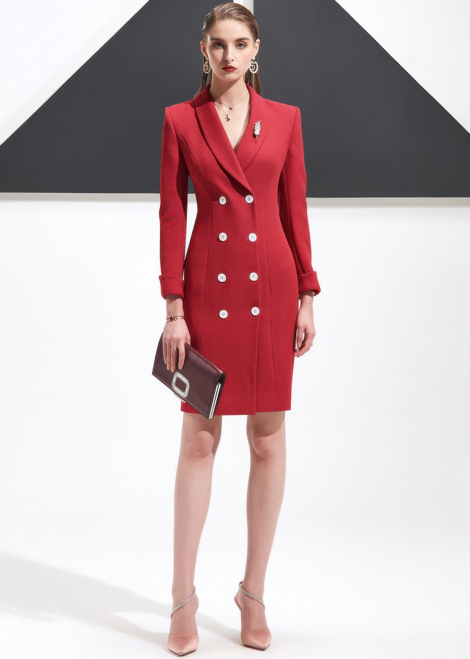 A full-length shot of a woman in a red shawl lapel blazer dress, holding a clutch and wearing light-colored heels.