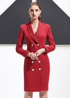 A medium shot of a woman in a red double-breasted blazer dress with her hands folded in front.