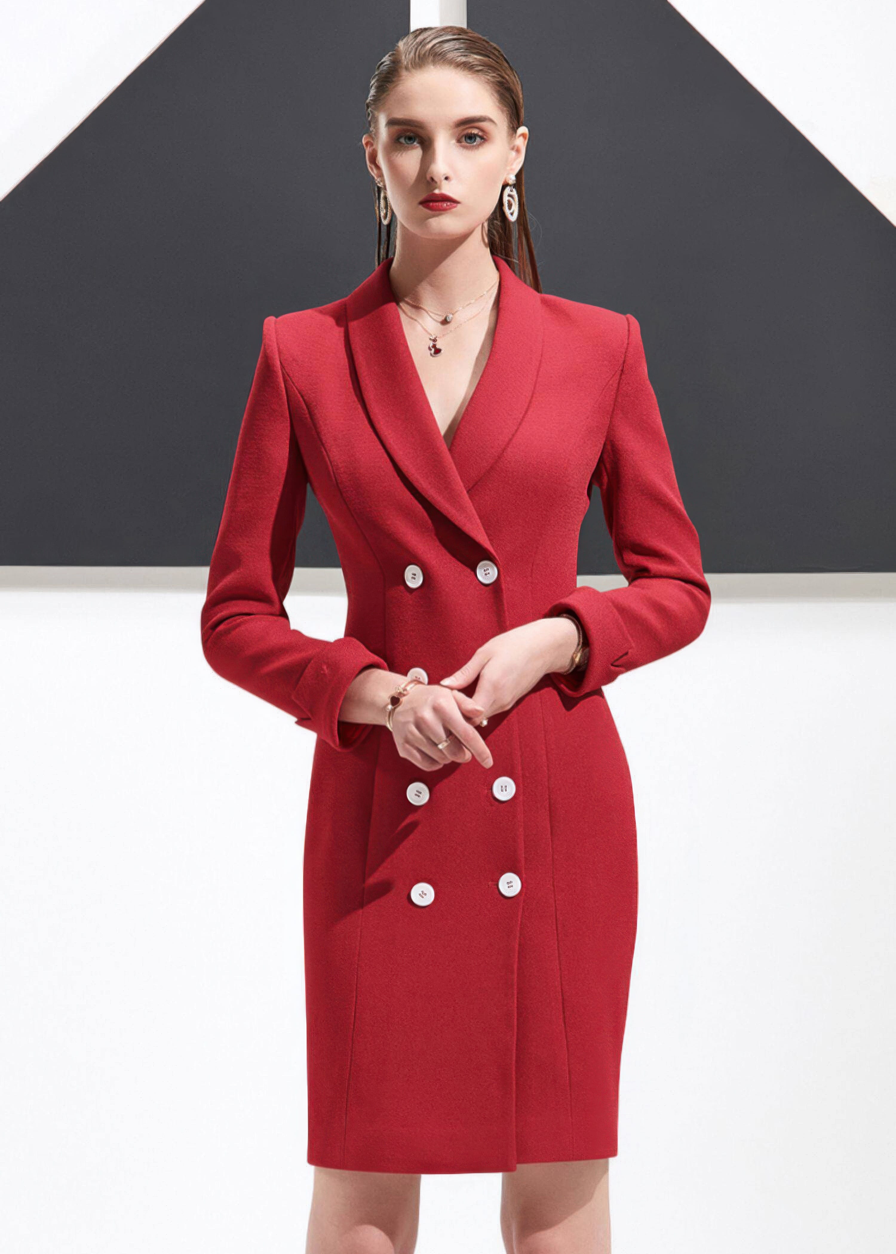 A medium shot of a woman in a red double-breasted blazer dress with her hands folded in front.