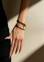 Side view of the women's sculptural hollow gold metal cuff bracelet on a wrist, featuring a wide, bold architectural silhouette.