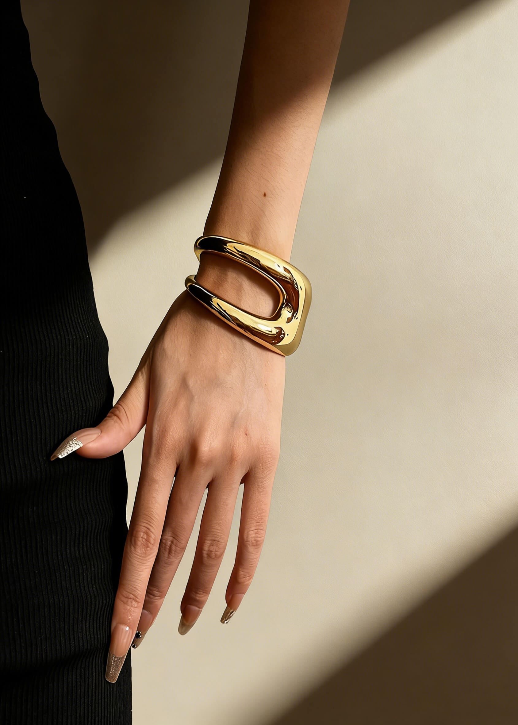 Side view of the women's sculptural hollow gold metal cuff bracelet on a wrist, featuring a wide, bold architectural silhouette.