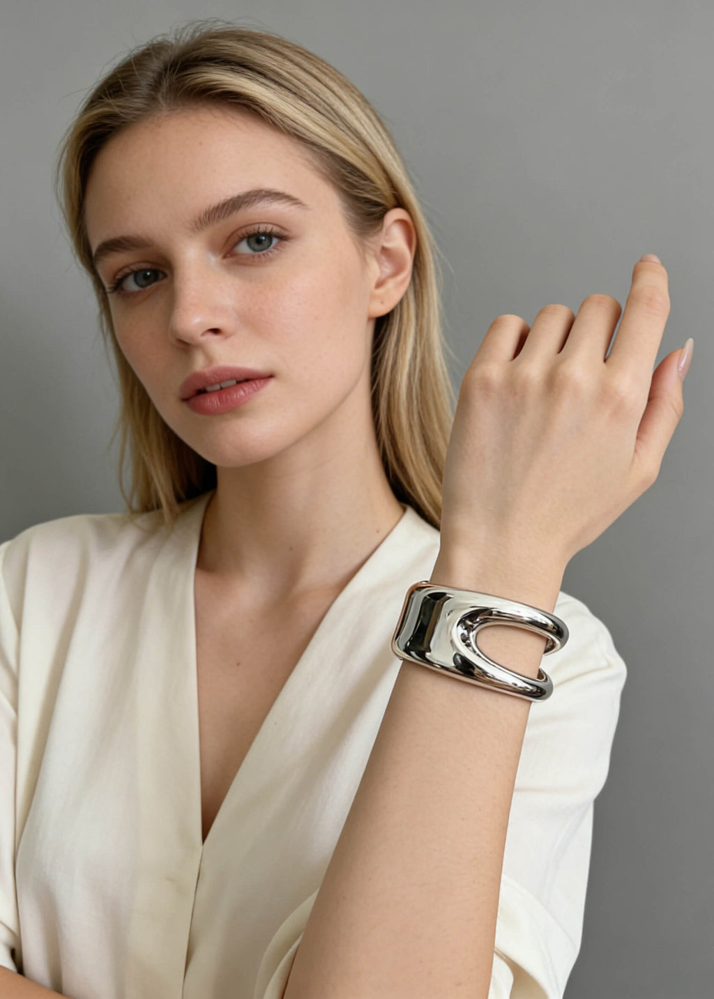 A blonde woman wearing a sculptural hollow silver cuff metal bracelet on her wrist, styled with a white V-neck top.