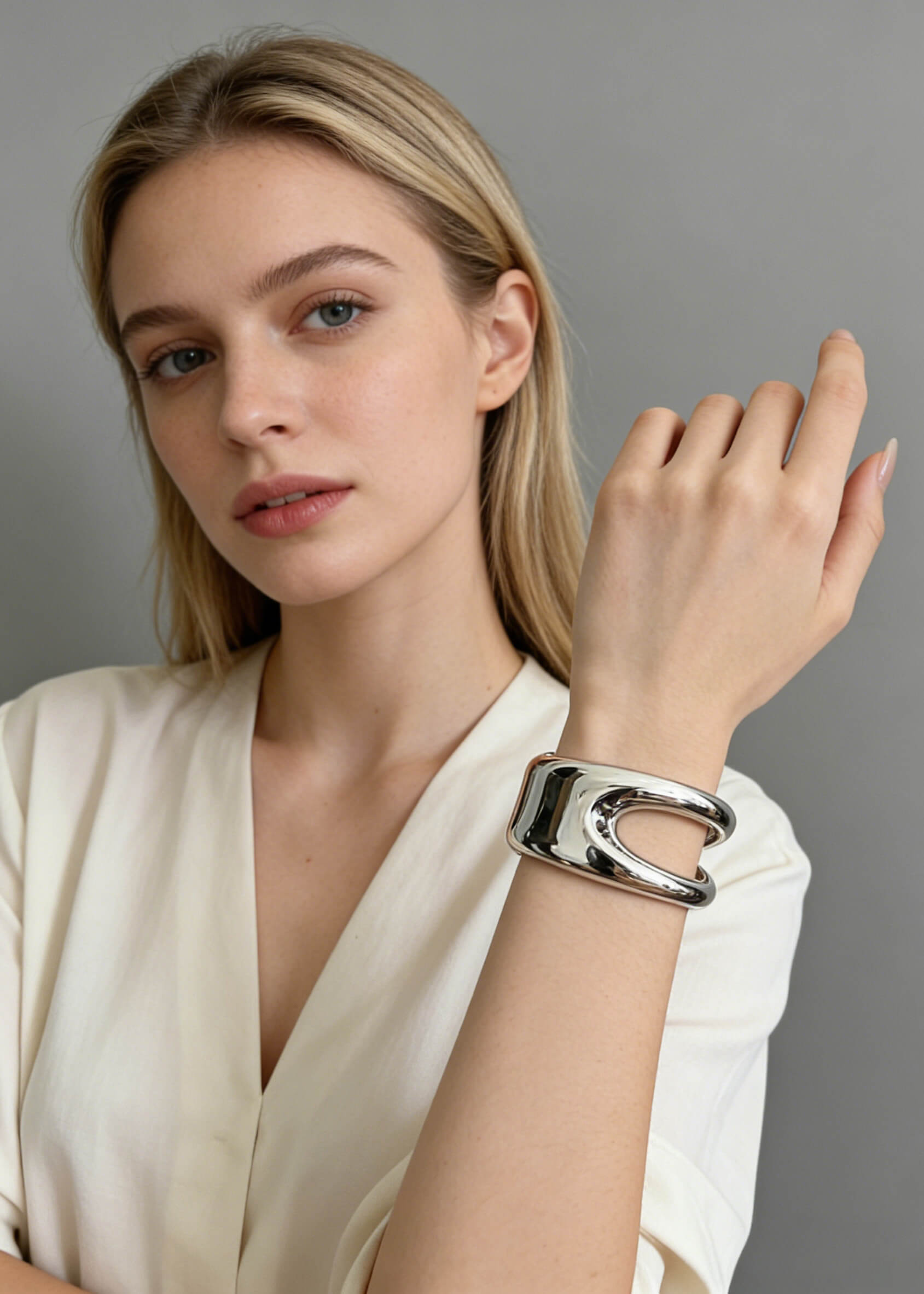 A blonde woman wearing a sculptural hollow silver cuff metal bracelet on her wrist, styled with a white V-neck top.