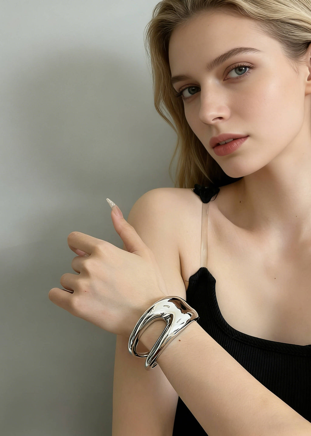 Close-up of a high-shine silver sculptural hollow cuff bracelet on a model’s wrist, showcasing the modern, fluid metal design.
