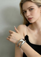 Close-up of a high-shine silver sculptural hollow cuff bracelet on a model’s wrist, showcasing the modern, fluid metal design.