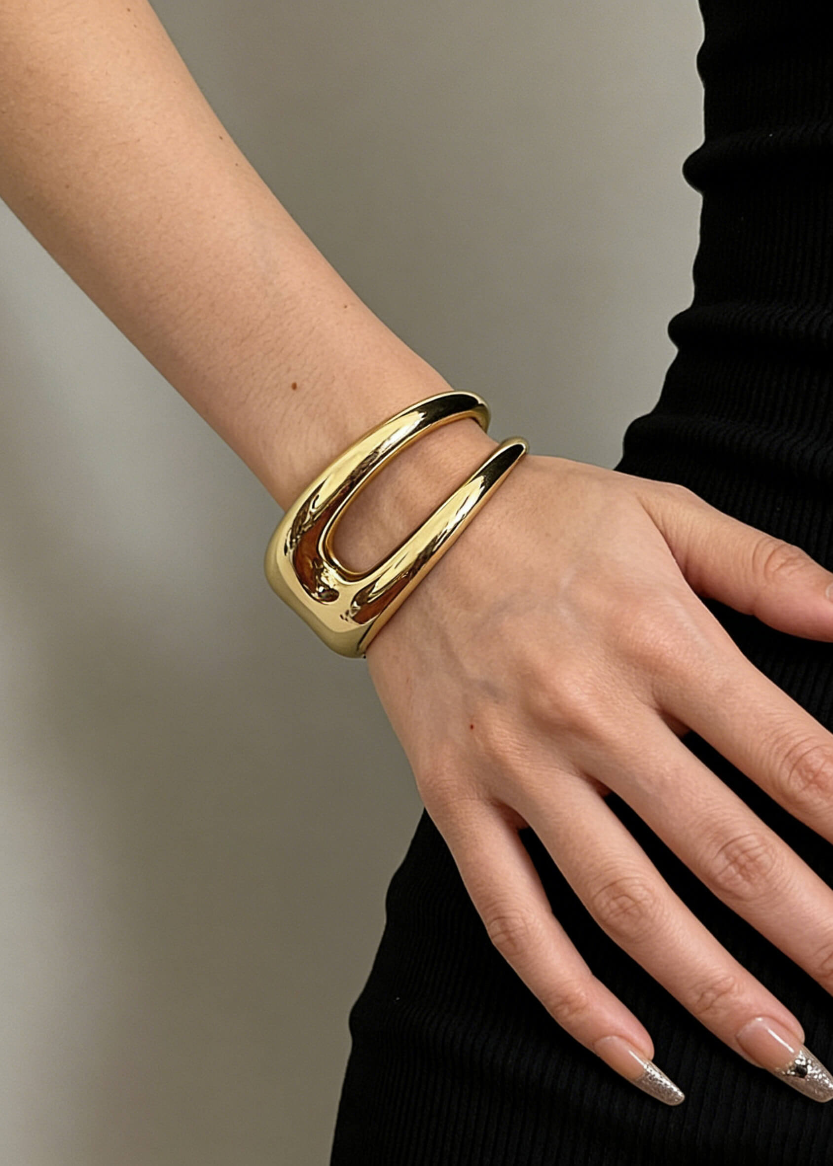 A polished gold sculptural hollow cuff bracelet worn on the arm, highlighting the smooth, reflective finish and unique open-center design.