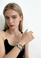 A blonde model wearing a chunky silver sculptural hollow cuff metal bracelet, demonstrating a chic and contemporary jewelry look.