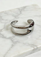Still life of a silver sculptural hollow cuff metal bracelet resting on a white marble surface to show texture and polish.