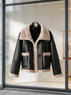 Front view of a black leather shearling-lined aviator jacket displayed on a hanger in boutique window