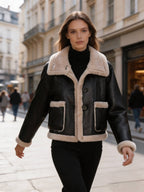 Woman walking down a city street wearing a cropped black leather aviator jacket with plush fleece lining