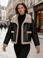 Model walking outdoors wearing a stylish cropped black leather jacket featuring contrast fur trim