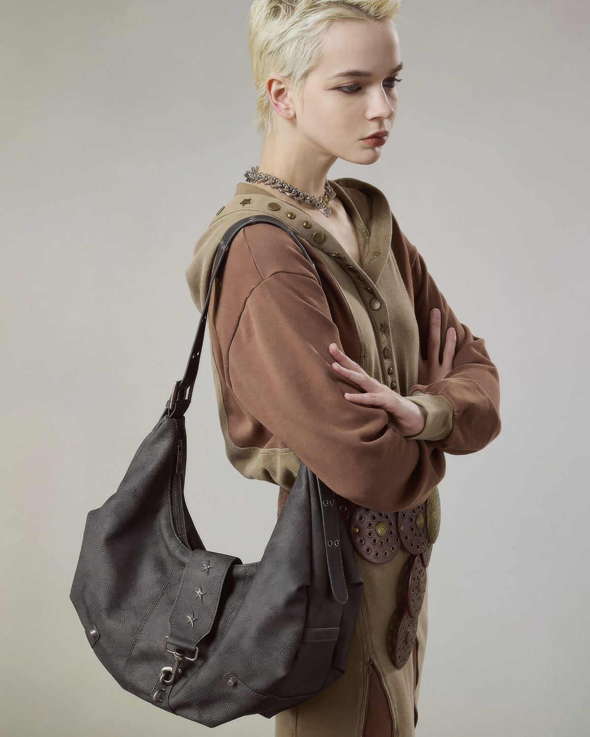Side view pose of model with short blonde hair carrying a dark grey distressed faux leather slouchy hobo purse