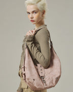 Model looking ahead while carrying a dusty pink slouchy crescent hobo shoulder bag with star metal studs